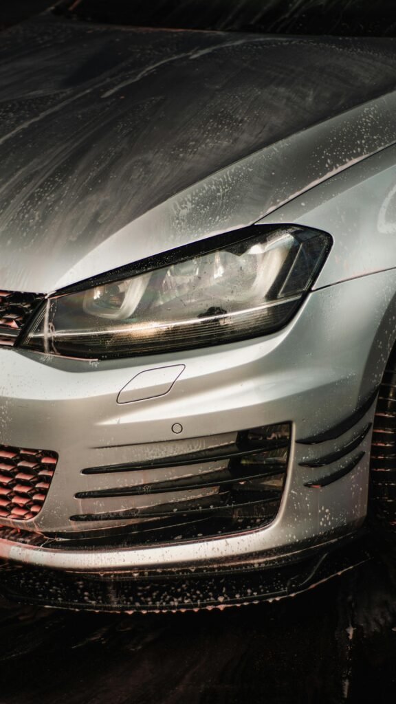 Detailed view of a silver car's front with droplets, highlighting chrome features.